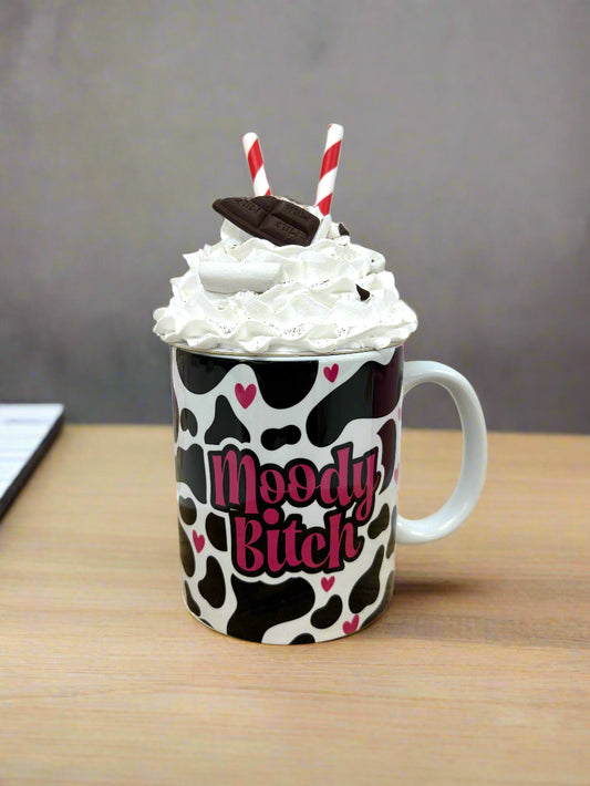 Mug with cow print and 'Moody Bitch' text, topped with whipped cream and straws.